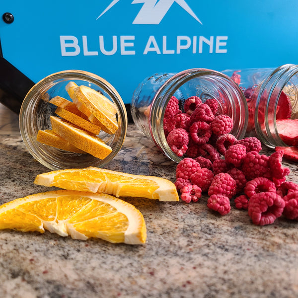 Home Freeze Dried Oranges, Raspberries, and Strawberries in jars in front of Blue Alpine Freeze Dryer